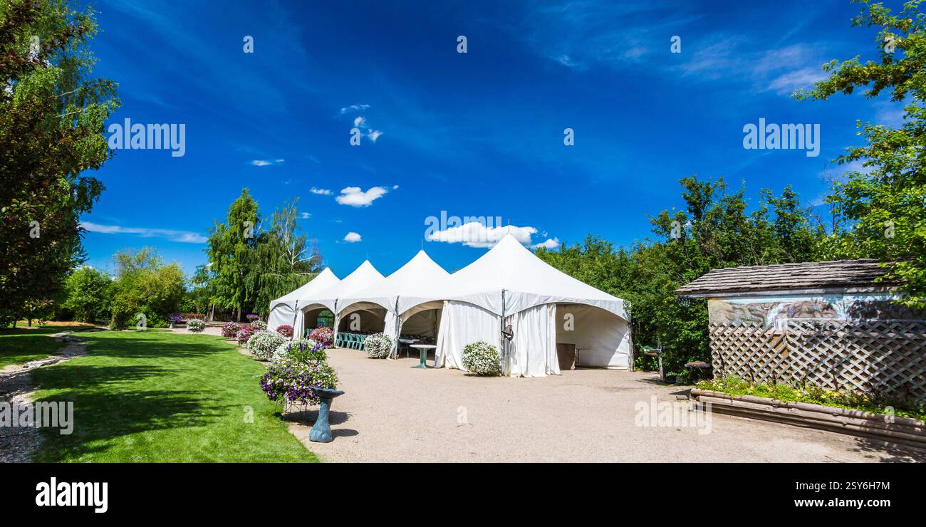 Großes weißes Zelt ist auf einem Feld aufgestellt. Es gibt mehrere Tische und Stühle um das Zelt herum Stockfoto