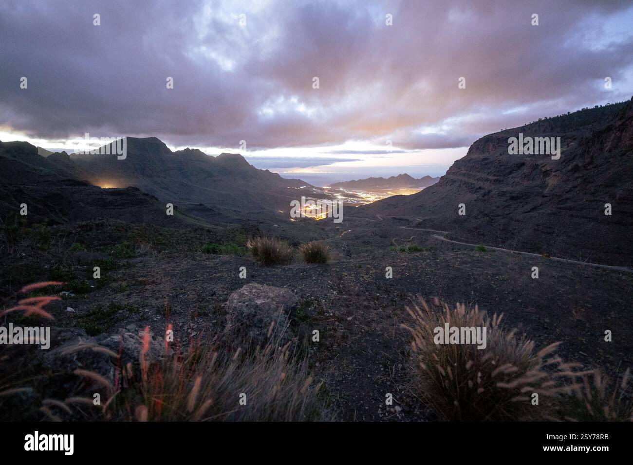 Ein Bergtal in der Abenddämmerung mit einer hellen Stadt und stürmischen Wolken Stockfoto