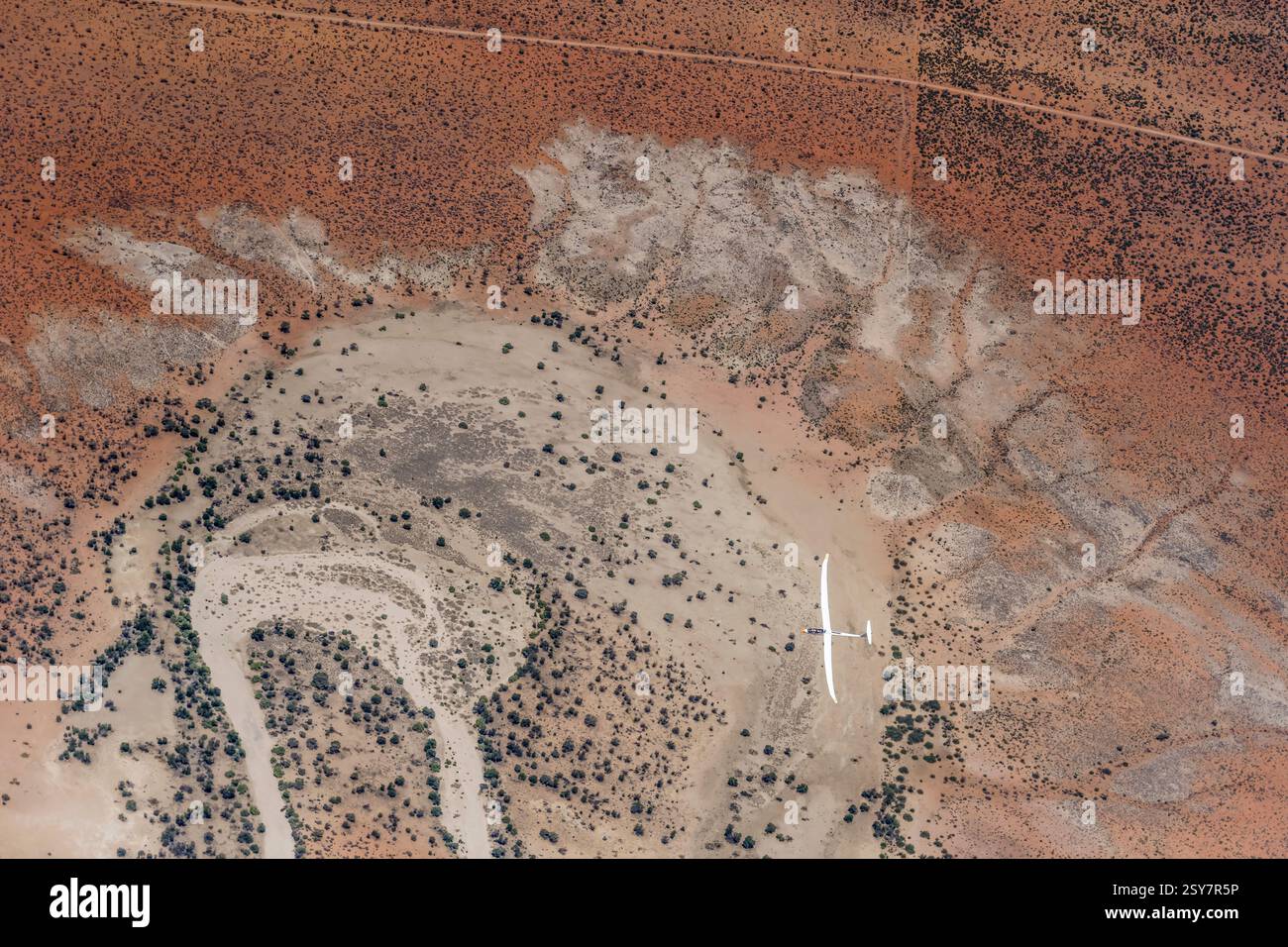 Luftlandschaft mit Segelflugzeug im Flug, die sich über trockenem Flussbett in der roten Kalahari-Wüste dreht, von einem anderen Segelflugzeug in hellem Spätlicht aufgenommen Stockfoto
