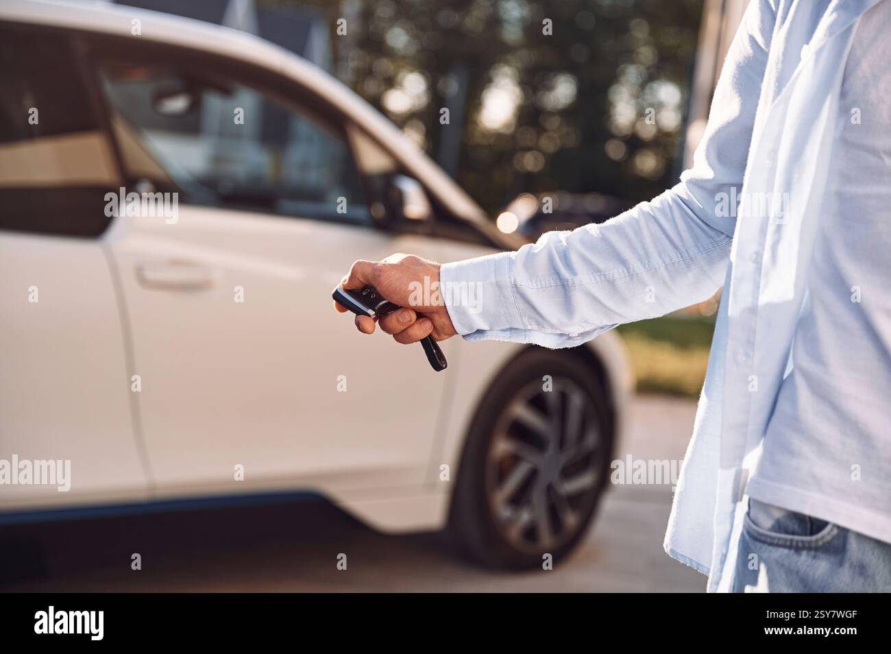 Mit den Schlüsseln stehen und das Auto verriegeln. Nahaufnahme eines Mannes mit seinem Elektroauto. Stockfoto