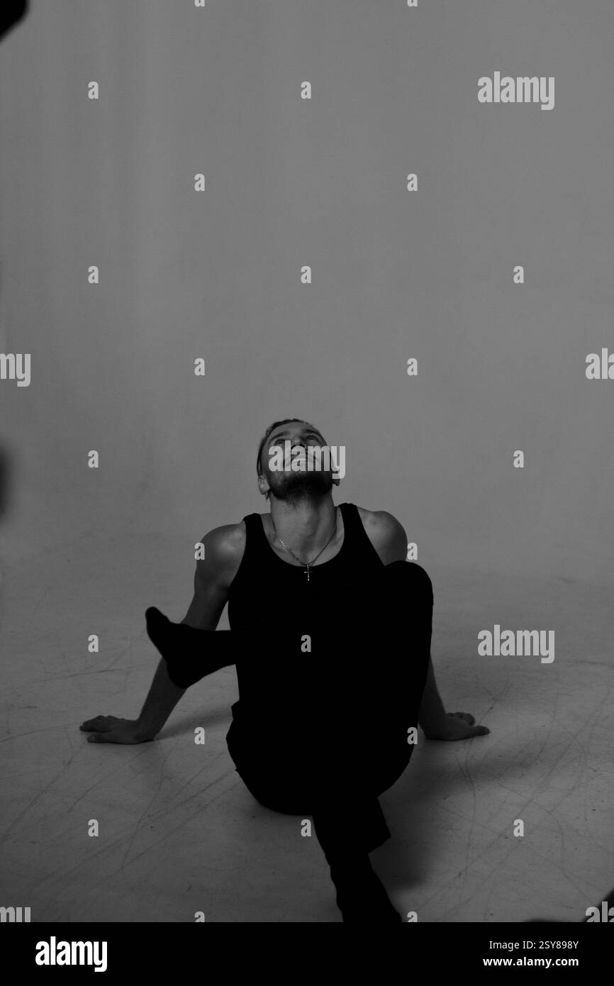 Eine Person in einem Tanktop sitzt auf dem Boden, Kopf nach hinten geneigt, in einer minimalistischen Umgebung Stockfoto Eine Person in einem Tanktop sitzt auf dem Boden, Kopf nach hinten geneigt, in einer minimalistischen Umgebung Stockfoto