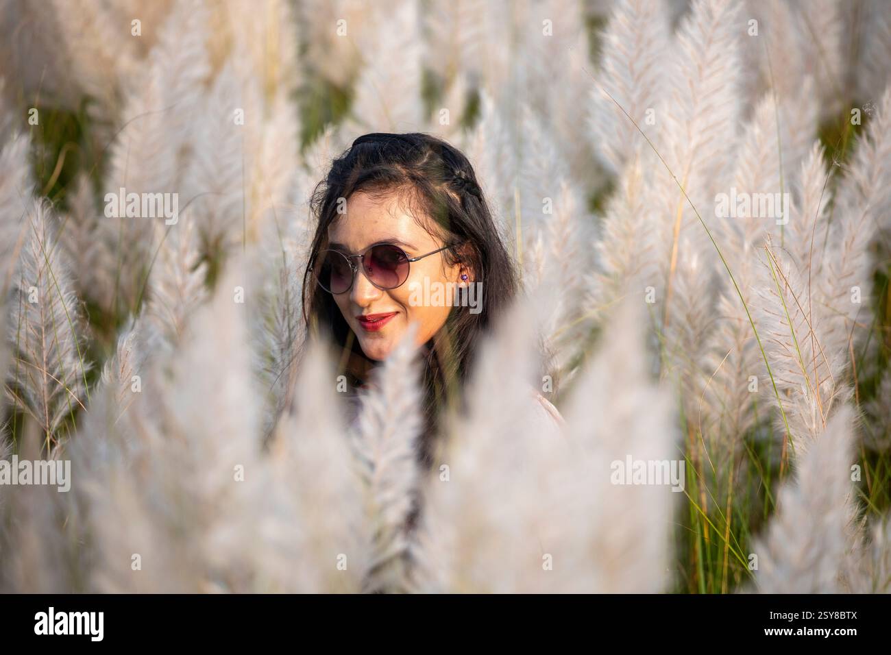 Eine fröhliche junge Frau genießt die Schönheit der blühenden Kans-Grasblumen, die das Wesen des Herbstes am Stadtrand von Dhaka, Bangladesch, genießen. Stockfoto