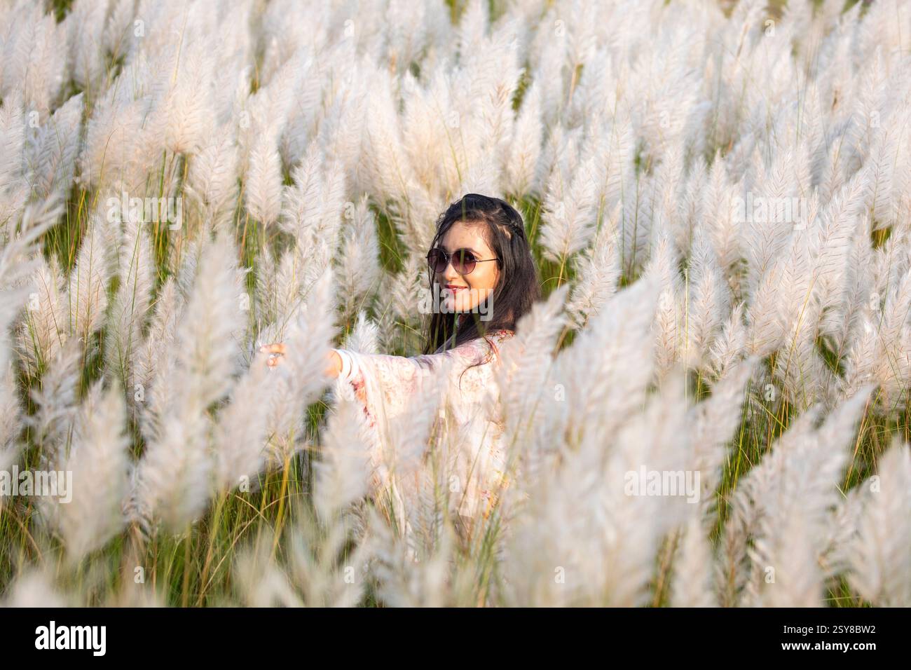Eine fröhliche junge Frau genießt die Schönheit der blühenden Kans-Grasblumen, die das Wesen des Herbstes am Stadtrand von Dhaka, Bangladesch, genießen. Stockfoto