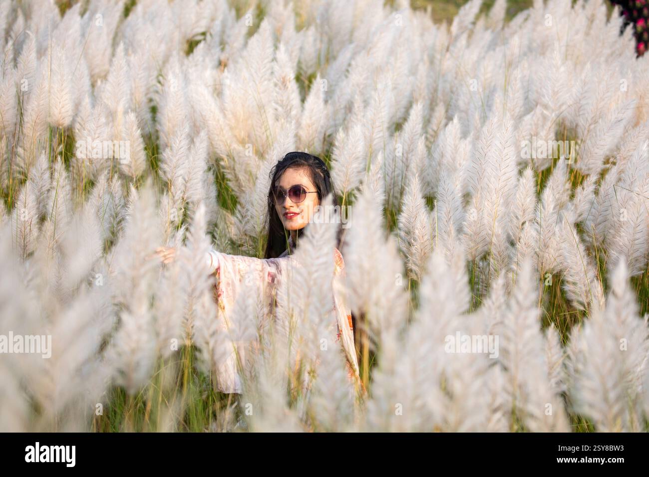 Eine fröhliche junge Frau genießt die Schönheit der blühenden Kans-Grasblumen, die das Wesen des Herbstes am Stadtrand von Dhaka, Bangladesch, genießen. Stockfoto