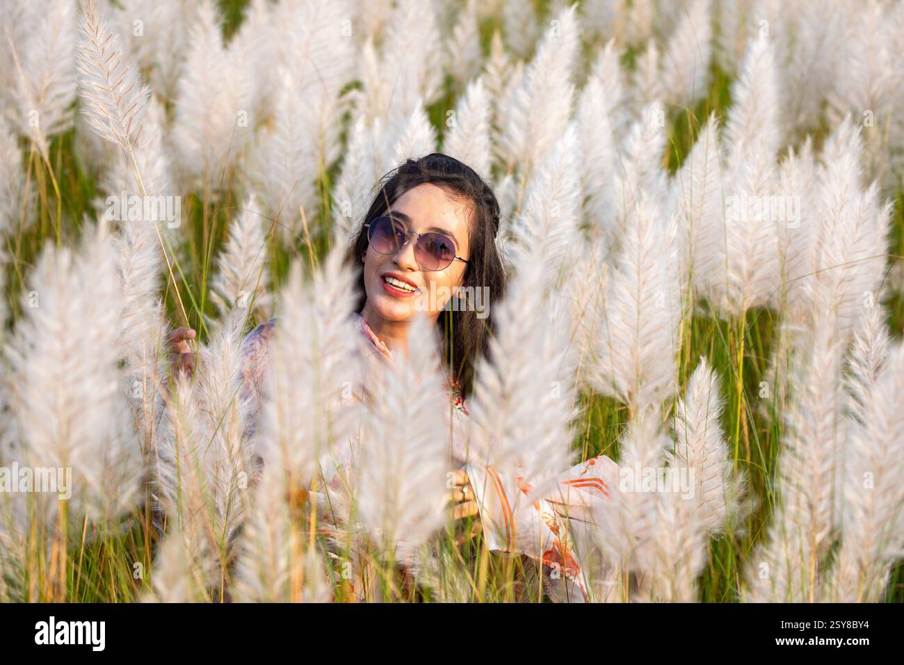 Eine fröhliche junge Frau genießt die Schönheit der blühenden Kans-Grasblumen, die das Wesen des Herbstes am Stadtrand von Dhaka, Bangladesch, genießen. Stockfoto