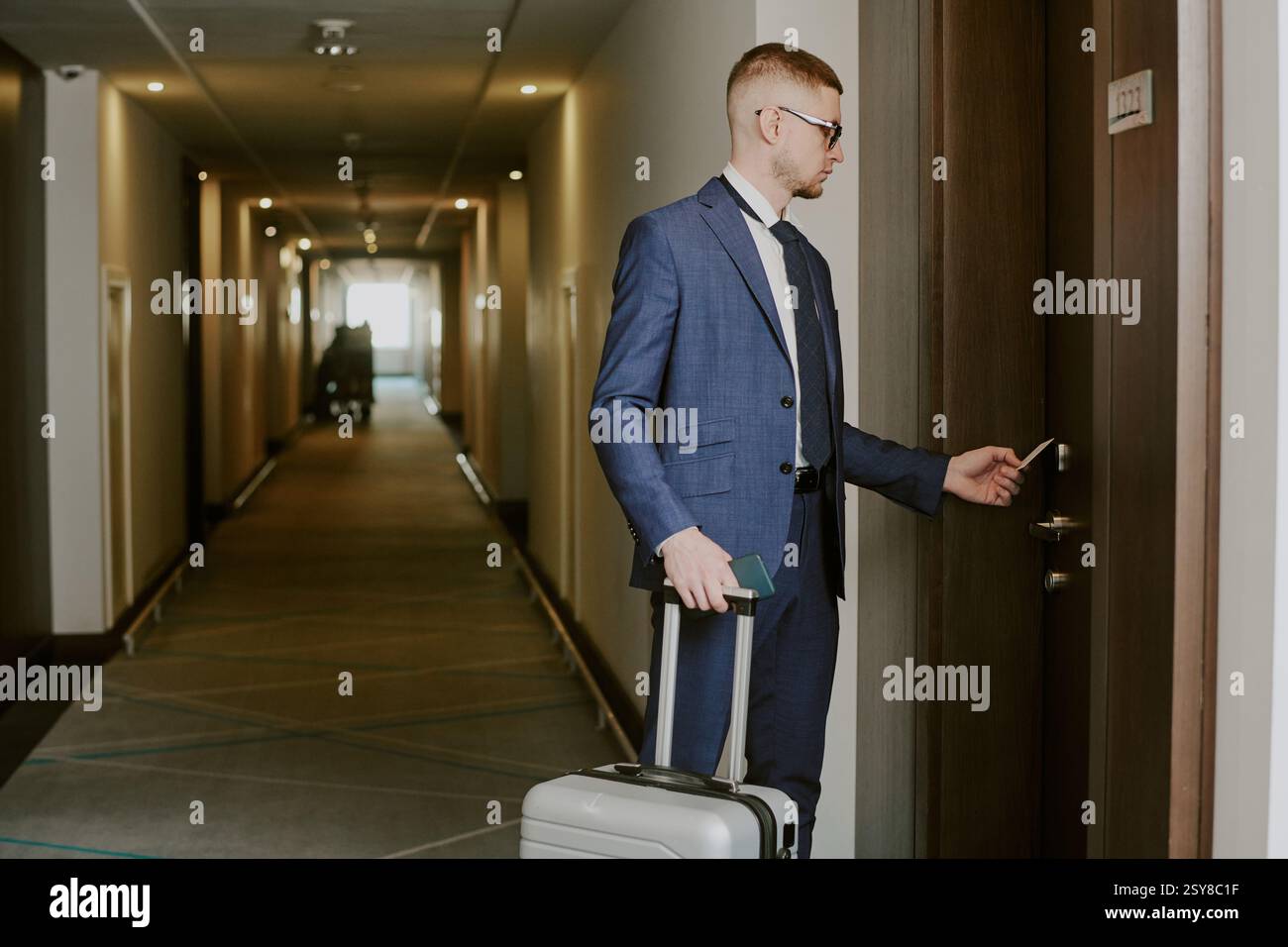 Mittlere Nahaufnahme eines gerade angekommenen Mannes mit silbernem Koffer, der vor der Tür stand und eine Karte benutzte, um sein Hotelzimmer zu öffnen Stockfoto