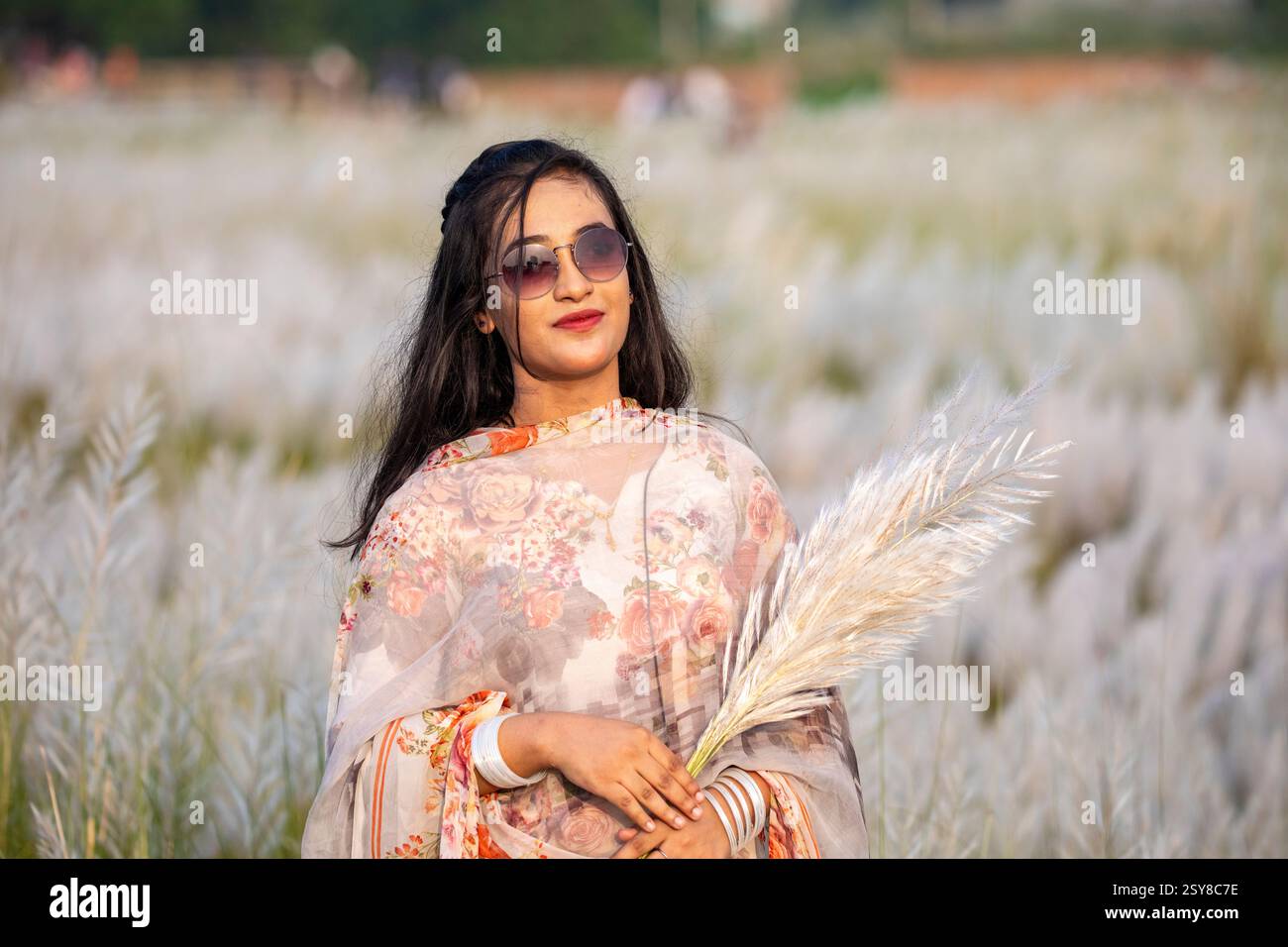 Eine fröhliche junge Frau genießt die Schönheit der blühenden Kans-Grasblumen, die das Wesen des Herbstes am Stadtrand von Dhaka, Bangladesch, genießen. Stockfoto