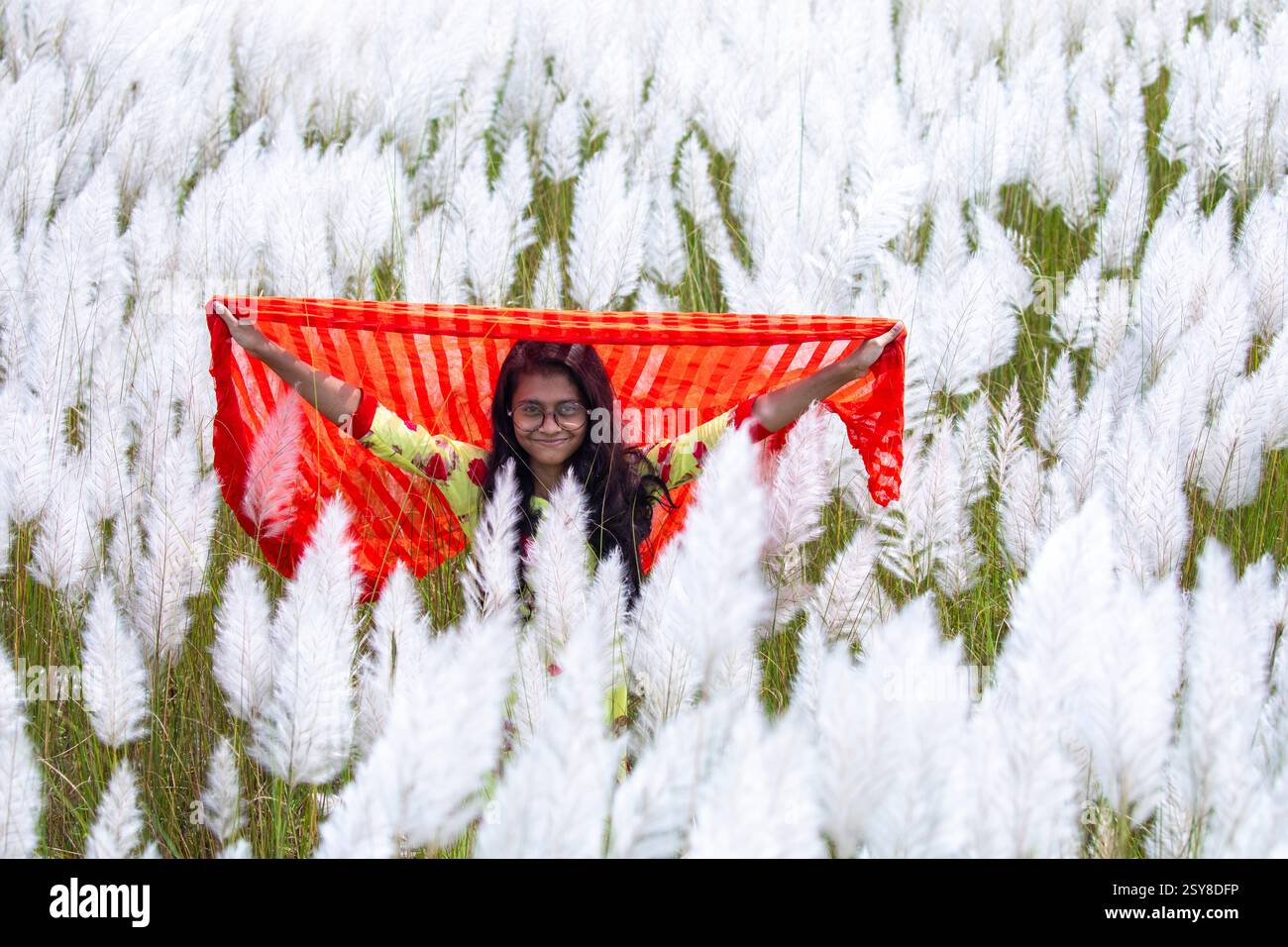 Eine fröhliche junge Frau genießt die Schönheit der blühenden Kans-Grasblumen, die das Wesen des Herbstes am Stadtrand von Dhaka, Bangladesch, genießen. Stockfoto