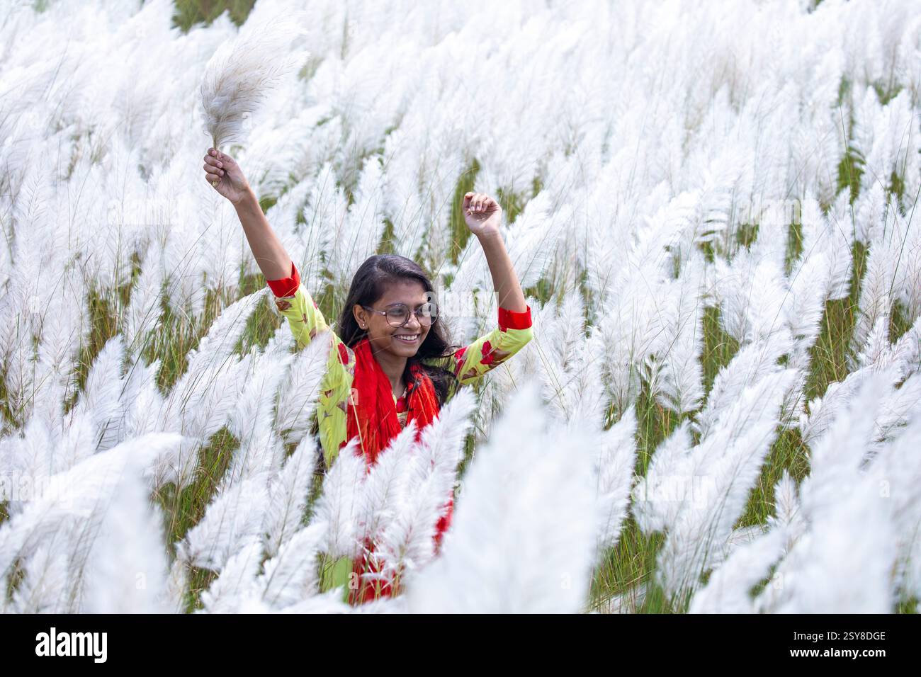 Eine fröhliche junge Frau genießt die Schönheit der blühenden Kans-Grasblumen, die das Wesen des Herbstes am Stadtrand von Dhaka, Bangladesch, genießen. Stockfoto