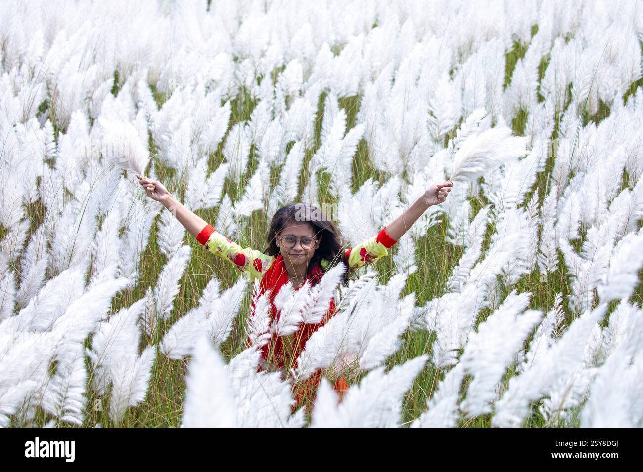 Eine fröhliche junge Frau genießt die Schönheit der blühenden Kans-Grasblumen, die das Wesen des Herbstes am Stadtrand von Dhaka, Bangladesch, genießen. Stockfoto