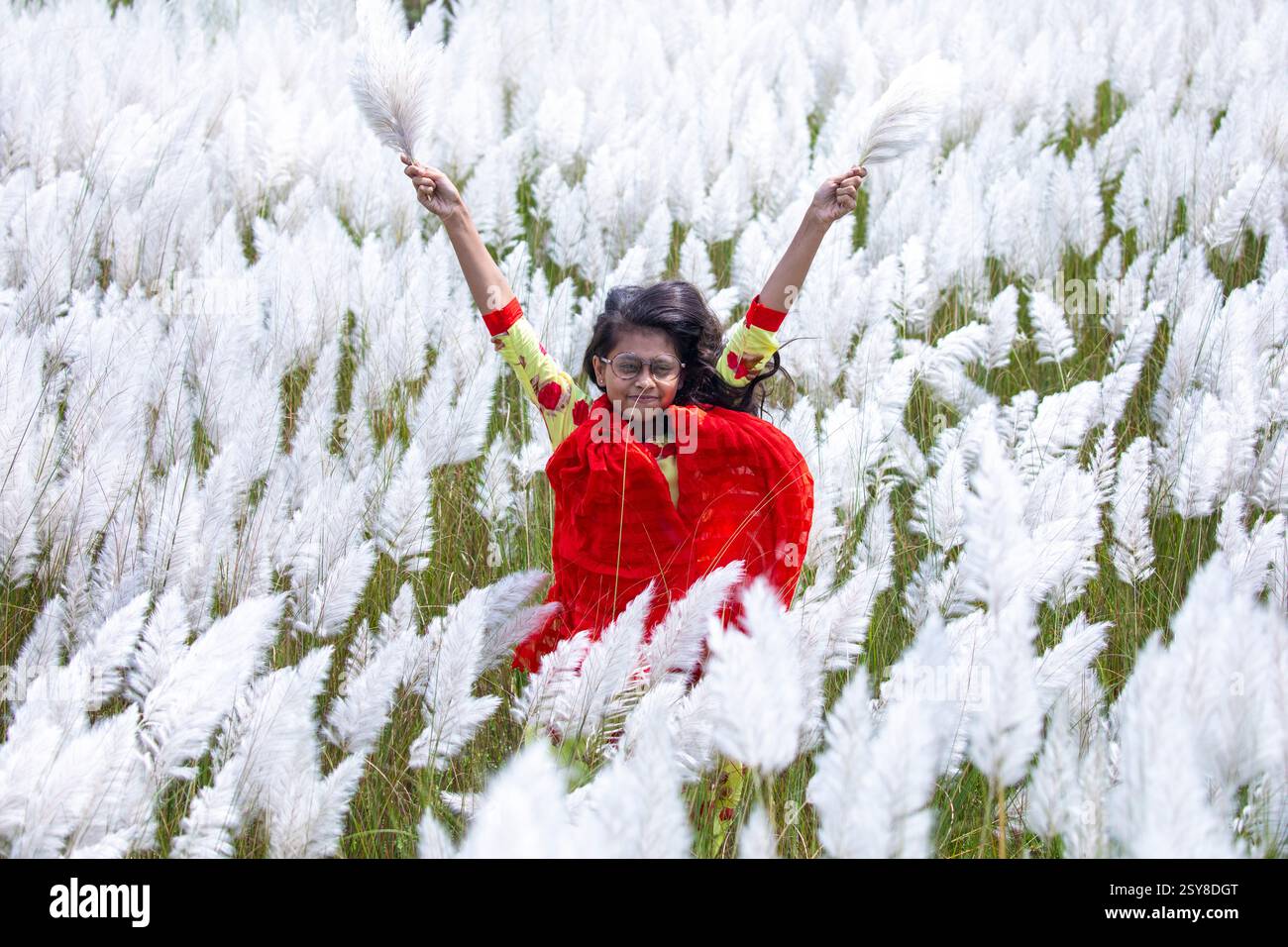 Eine fröhliche junge Frau genießt die Schönheit der blühenden Kans-Grasblumen, die das Wesen des Herbstes am Stadtrand von Dhaka, Bangladesch, genießen. Stockfoto