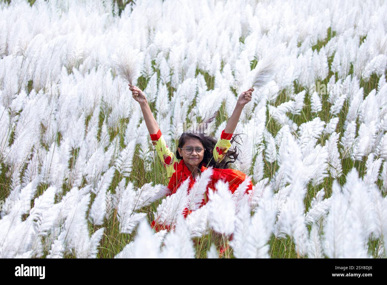 Eine fröhliche junge Frau genießt die Schönheit der blühenden Kans-Grasblumen, die das Wesen des Herbstes am Stadtrand von Dhaka, Bangladesch, genießen. Stockfoto