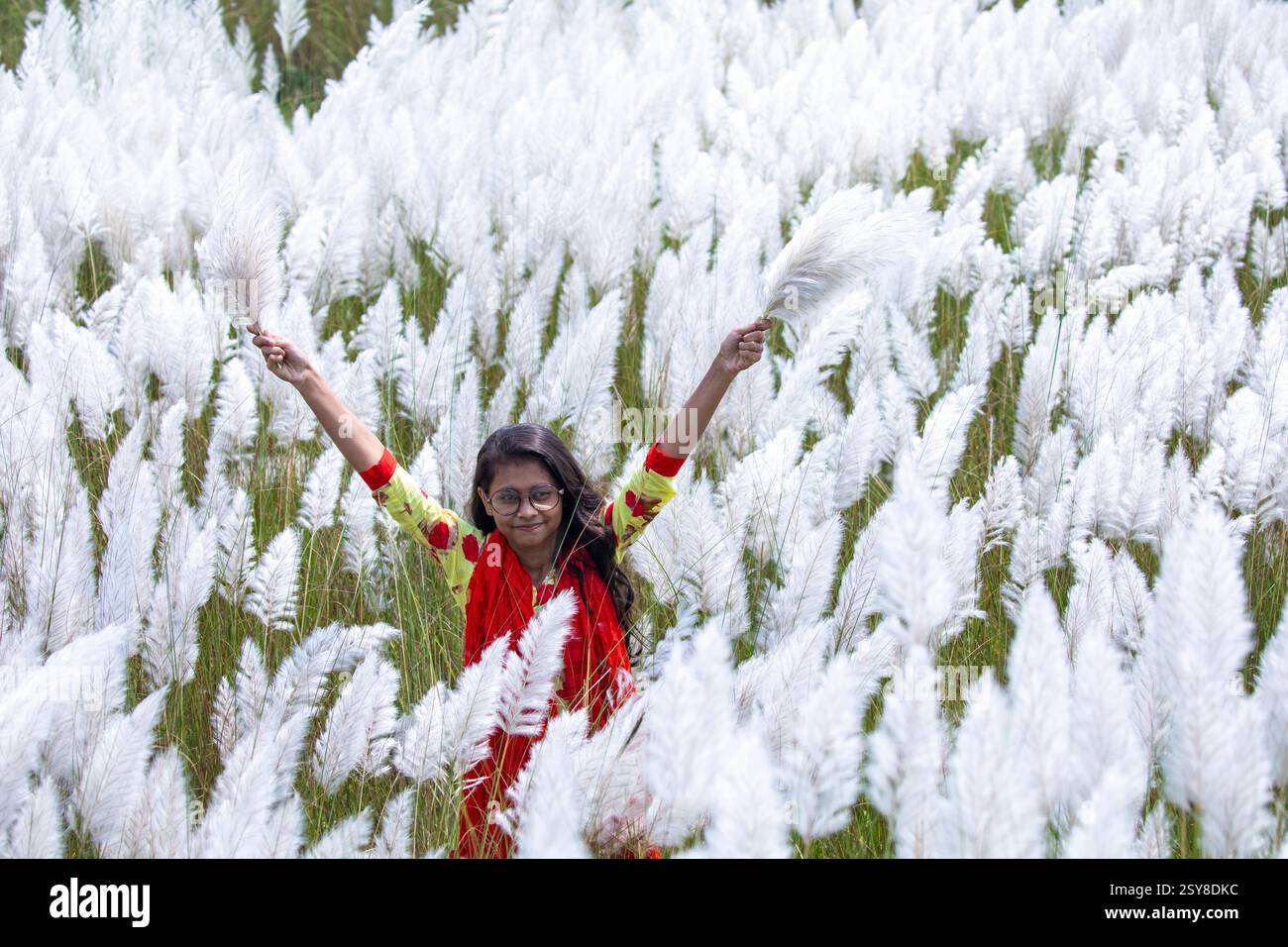 Eine fröhliche junge Frau genießt die Schönheit der blühenden Kans-Grasblumen, die das Wesen des Herbstes am Stadtrand von Dhaka, Bangladesch, genießen. Stockfoto