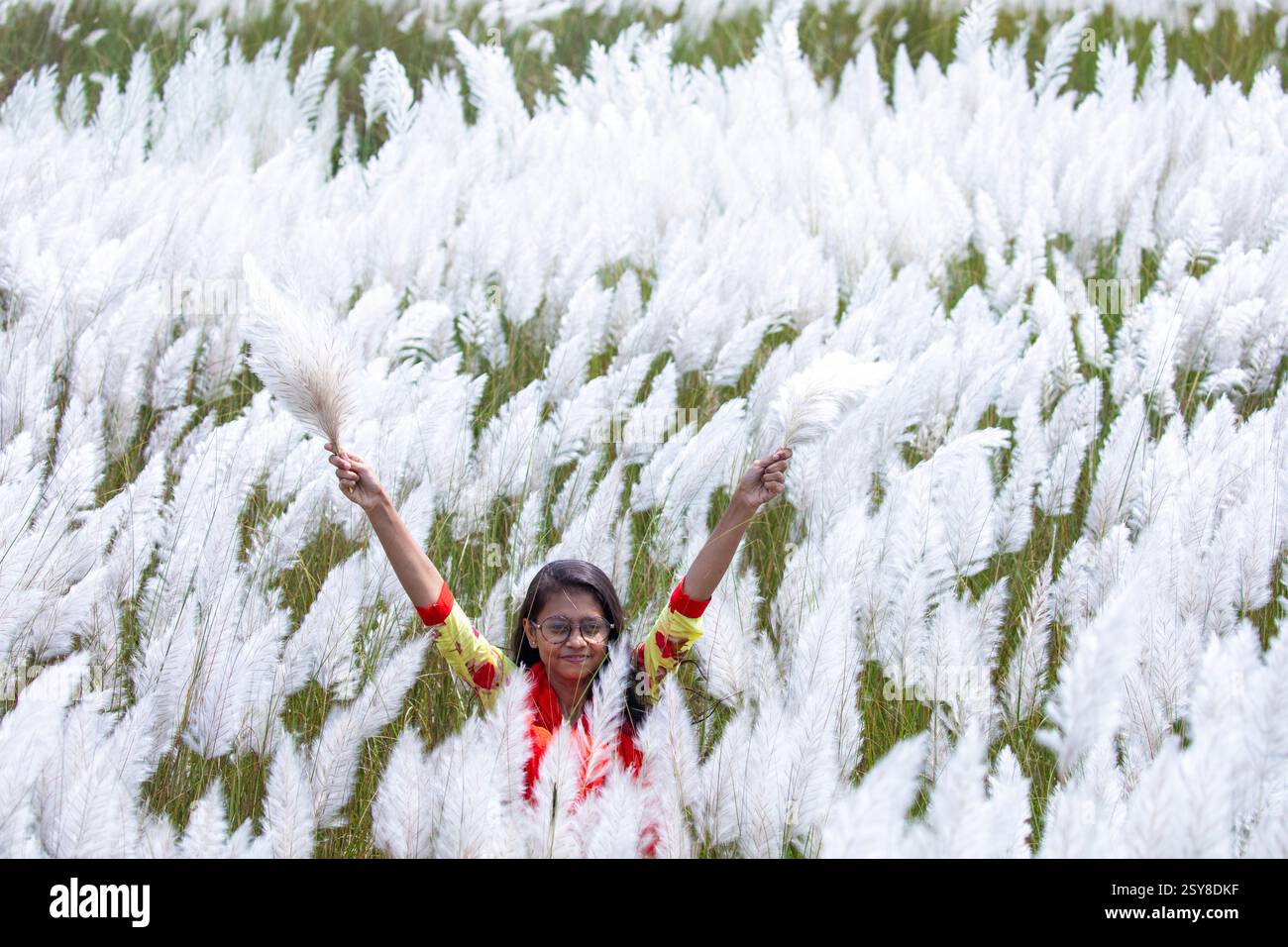 Eine fröhliche junge Frau genießt die Schönheit der blühenden Kans-Grasblumen, die das Wesen des Herbstes am Stadtrand von Dhaka, Bangladesch, genießen. Stockfoto