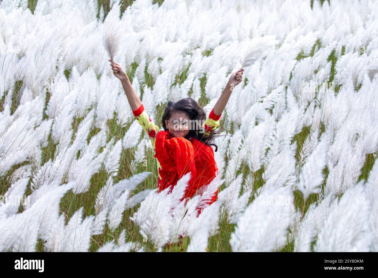 Eine fröhliche junge Frau genießt die Schönheit der blühenden Kans-Grasblumen, die das Wesen des Herbstes am Stadtrand von Dhaka, Bangladesch, genießen. Stockfoto