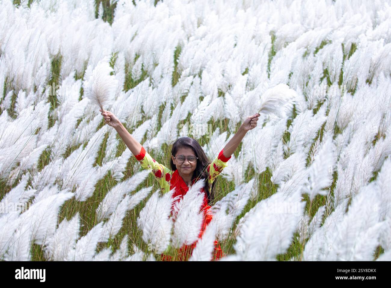Eine fröhliche junge Frau genießt die Schönheit der blühenden Kans-Grasblumen, die das Wesen des Herbstes am Stadtrand von Dhaka, Bangladesch, genießen. Stockfoto