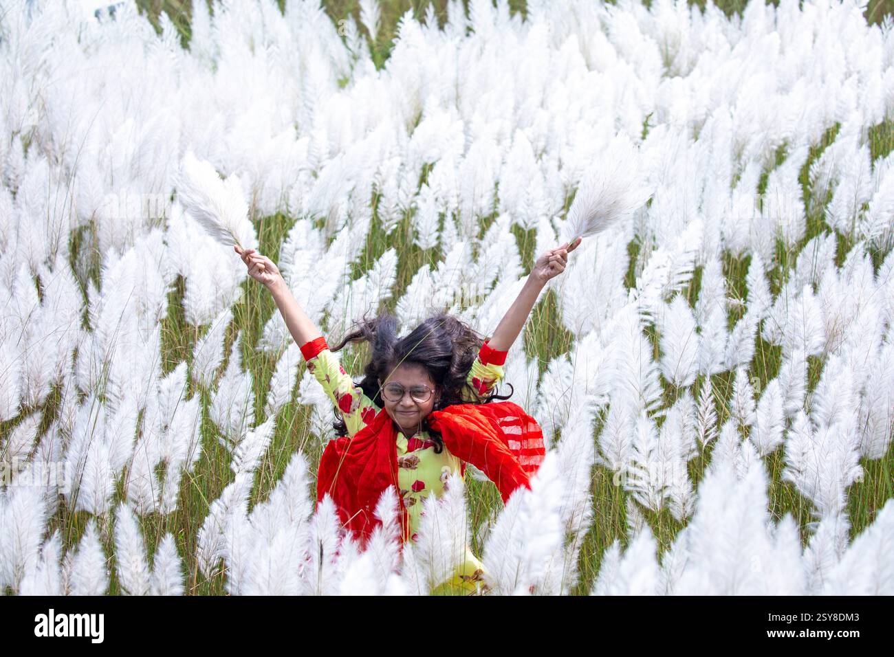 Eine fröhliche junge Frau genießt die Schönheit der blühenden Kans-Grasblumen, die das Wesen des Herbstes am Stadtrand von Dhaka, Bangladesch, genießen. Stockfoto