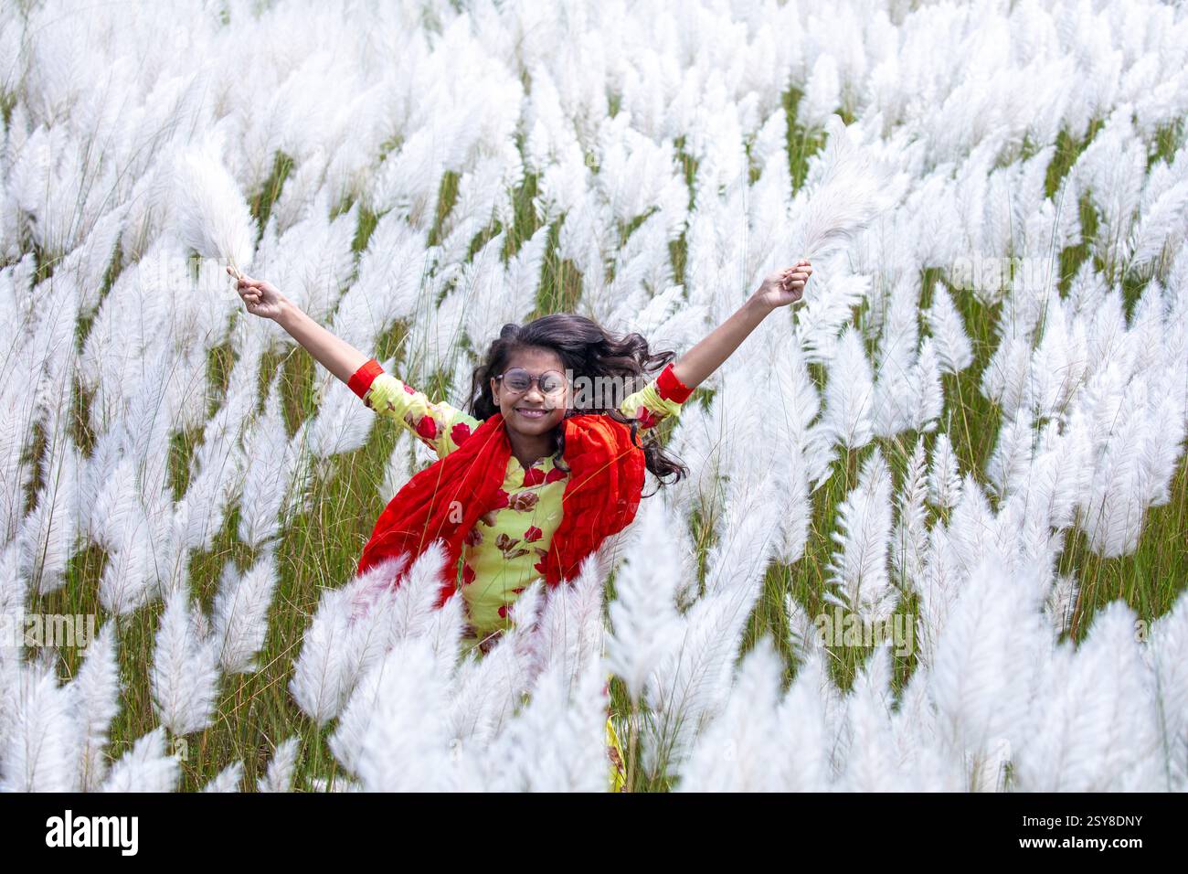 Eine fröhliche junge Frau genießt die Schönheit der blühenden Kans-Grasblumen, die das Wesen des Herbstes am Stadtrand von Dhaka, Bangladesch, genießen. Stockfoto