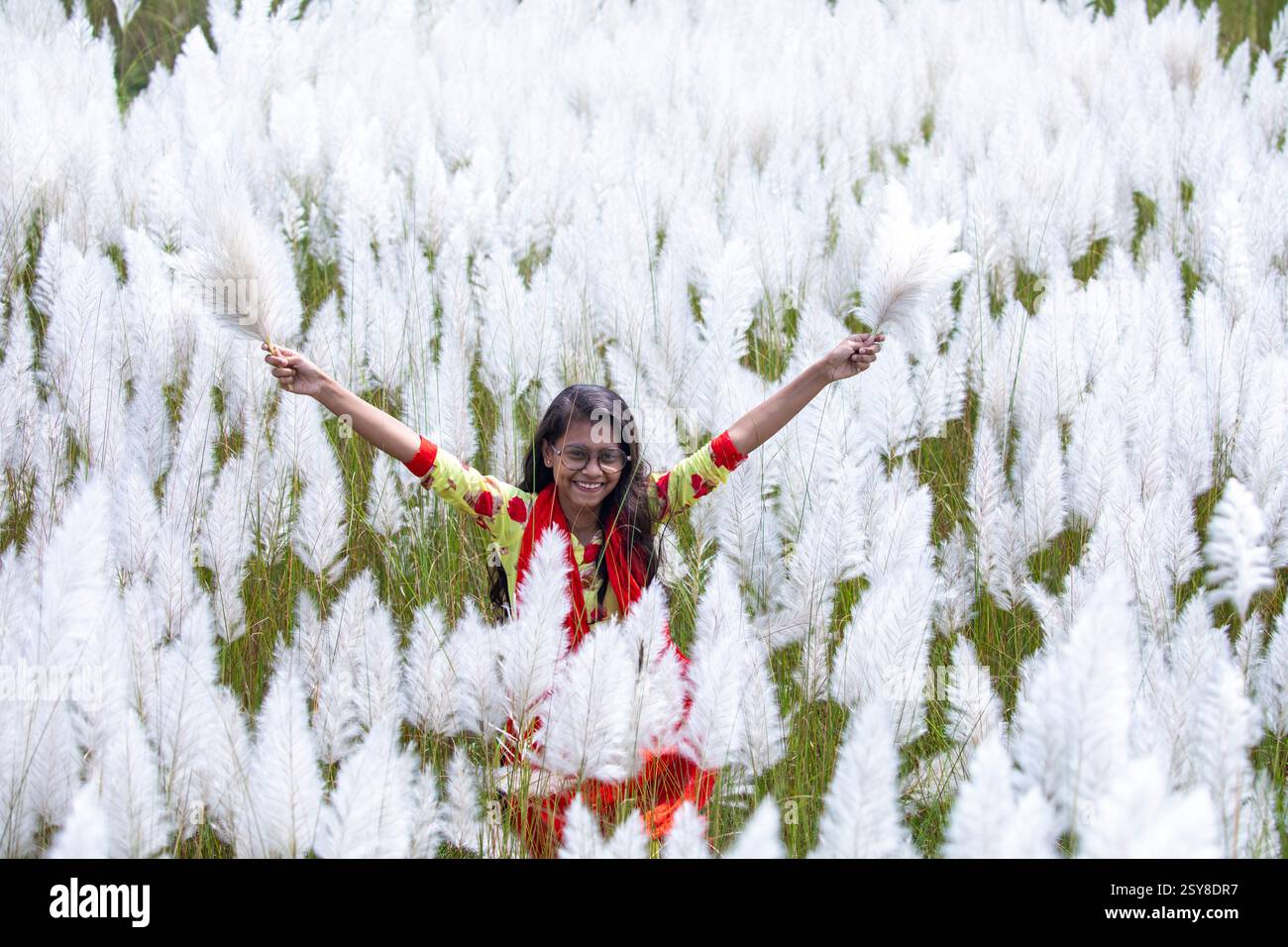 Eine fröhliche junge Frau genießt die Schönheit der blühenden Kans-Grasblumen, die das Wesen des Herbstes am Stadtrand von Dhaka, Bangladesch, genießen. Stockfoto
