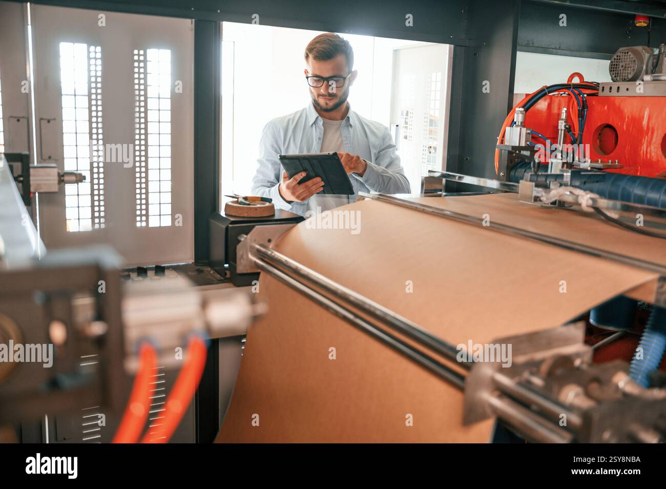 Halten des digitalen Tablets, wenn Sie in der Nähe der Blechschneidemaschine stehen. Der Arbeiter in weißen Kleidern ist drinnen. Stockfoto
