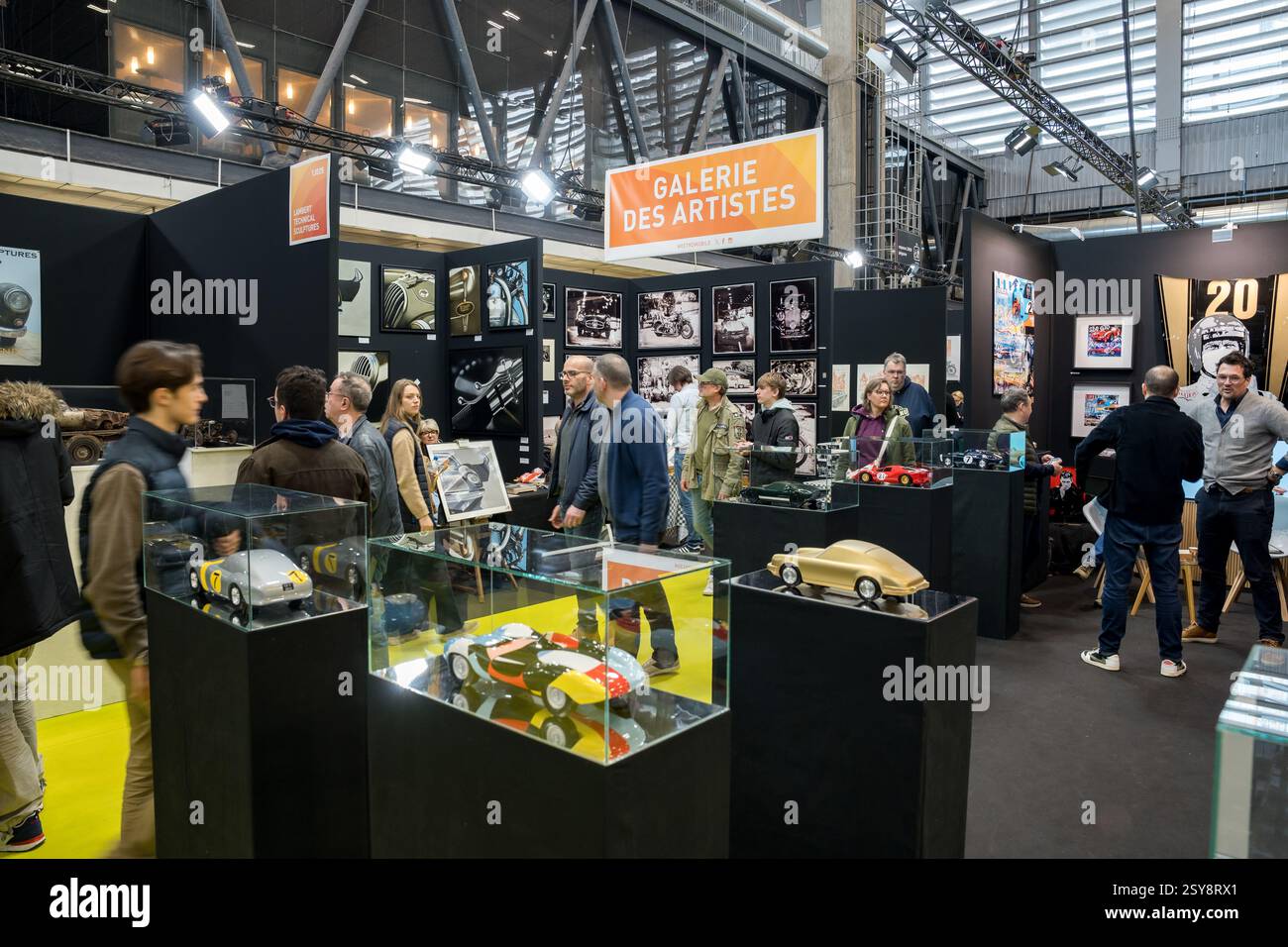 Besucher erkunden eine lebendige Kunstgalerie mit einzigartigen Automobildesigns auf einer geschäftigen Ausstellung in einem Industriebereich Stockfoto