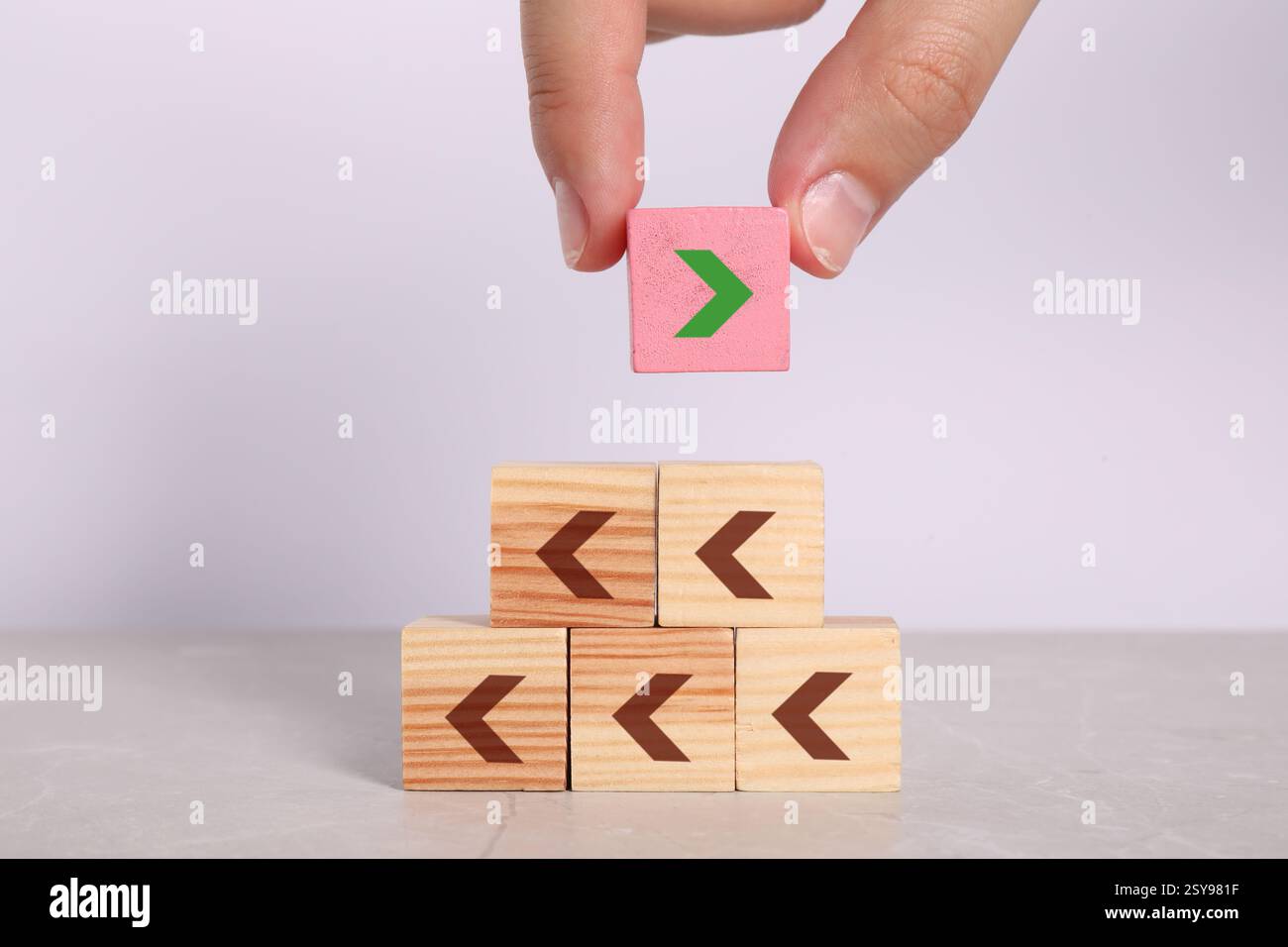 Frau, die einen rosafarbenen Würfel mit Pfeil auf die Pyramide legt, vor hellem Hintergrund, Nahaufnahme Stockfoto