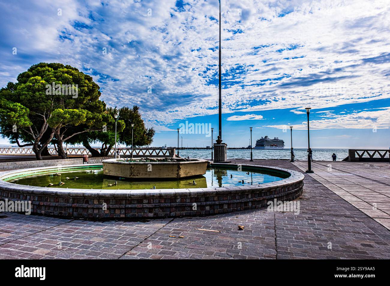 Puerto Madryn, Argentinien - 17. Dezember 2024: Springbrunnen am Ufer des Parks mit Kreuzfahrtschiff im Hintergrund. Stockfoto