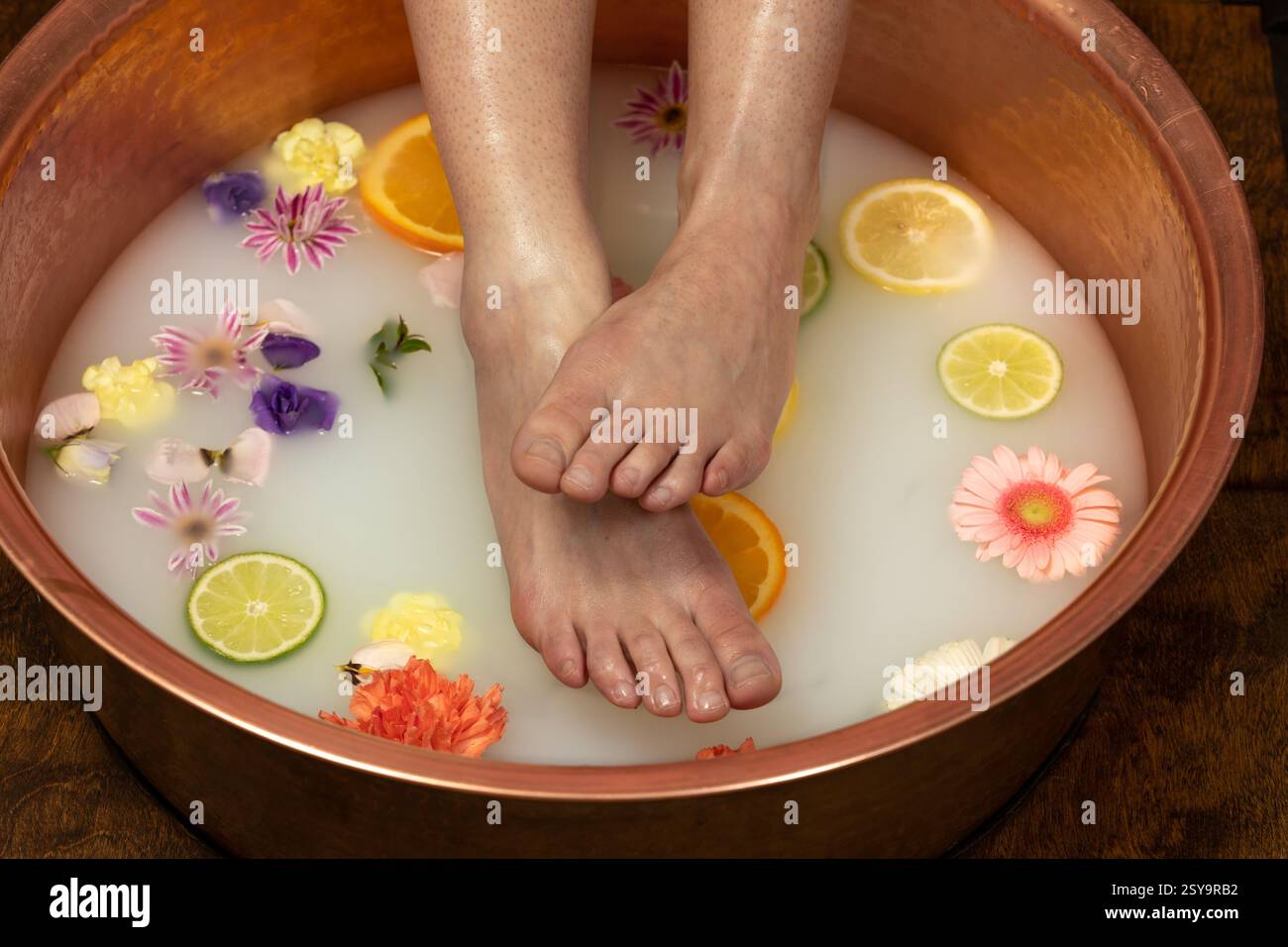 Füße in milchigen Fußbad mit Blumen und Scheiben geschnittenen Früchten, Kerzen und Kristall Stockfoto