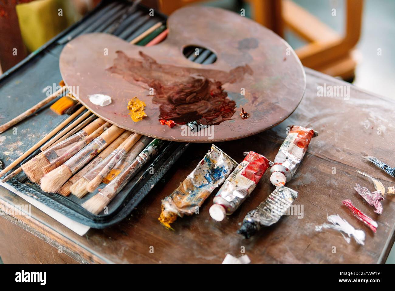 Eine Holzpalette mit gemischten Farben liegt auf einem Karton mit Pinseln, mit gebrauchten Farbtuben in der Nähe. Die Szene beleuchtet den künstlerischen Prozess und das To Stockfoto