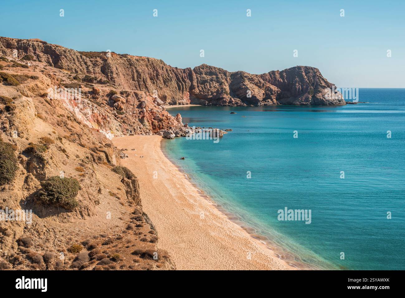 Entdecken Sie den Strand Paleochori auf der Insel Milos, Griechenland, mit seinem goldenen Sand und kristallklarem türkisfarbenem Wasser, umgeben von zerklüfteten Klippen unter einem leuchtenden blau Stockfoto