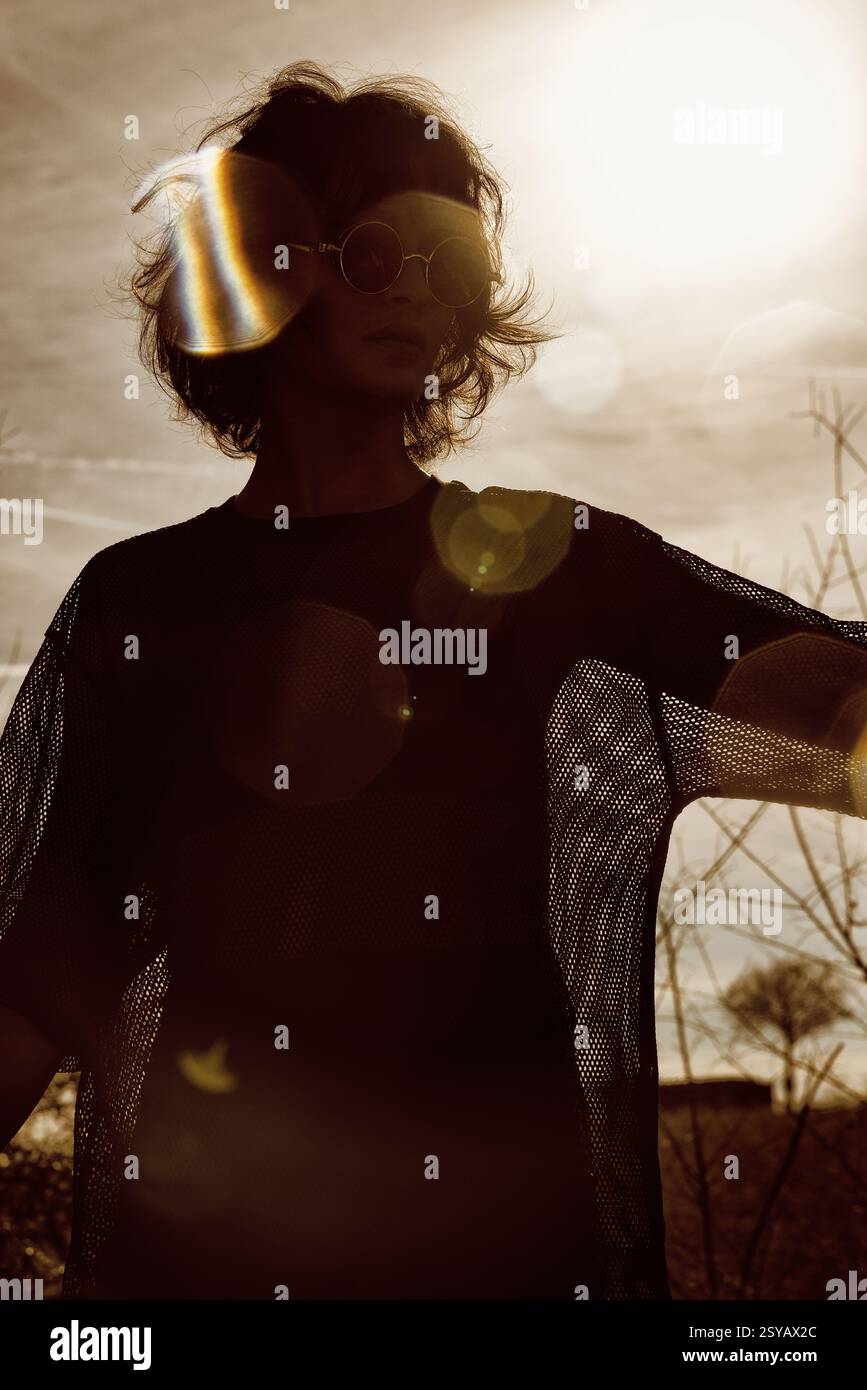 Porträt einer Frau mit Sonnenbrille, Silhouette vor einer hellen Sonne. Das Licht erzeugt eine auffällige Lichtreflexion und ein Gefühl von Rätsel. Stockfoto