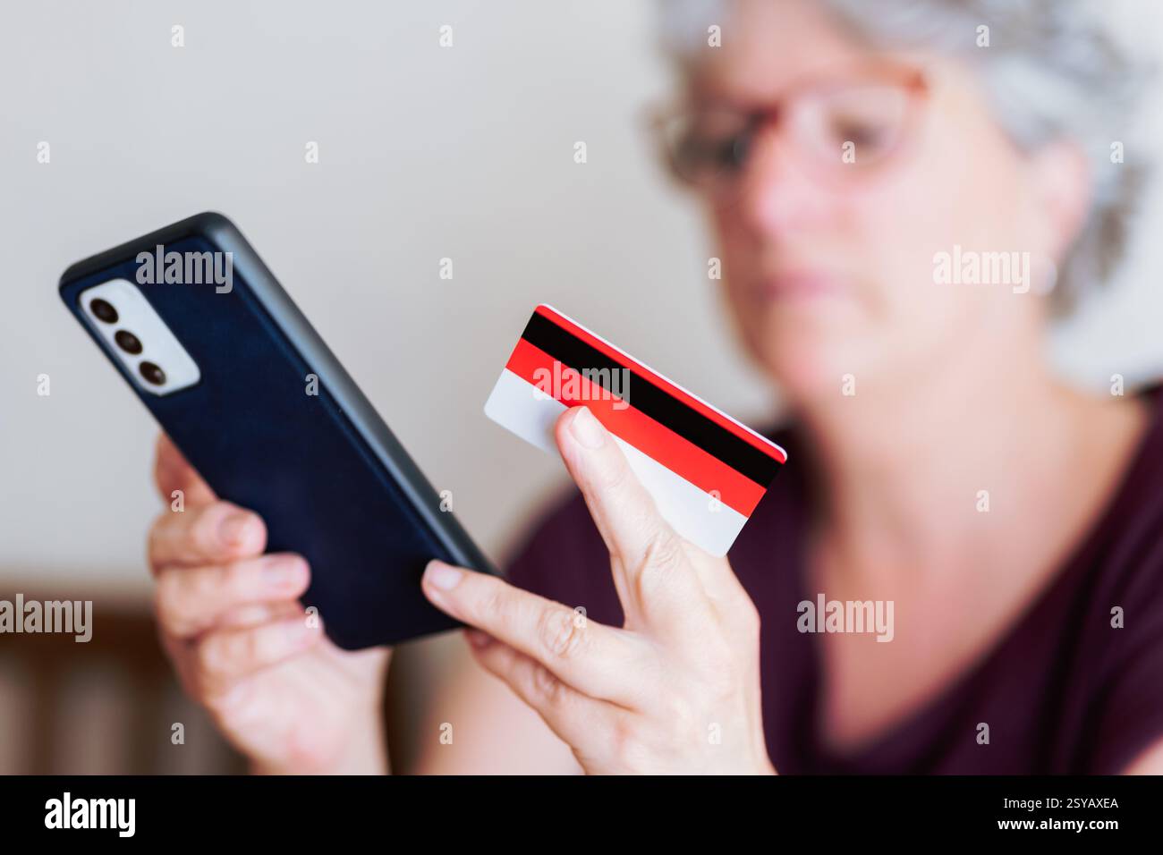 Eine Seniorin hat ein Smartphone und eine Kreditkarte, die Online-Shoppingaktivitäten macht. Das Bild zeigt den wachsenden Trend digitaler Transaktionen unter Stockfoto
