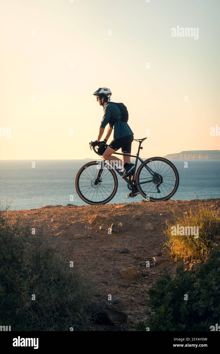 Ein junger Mann, der eine Radtour entlang der malerischen Küstenwege von Zahara de los Atunes in Cadiz bei einem wunderschönen Sonnenuntergang genießt. Stockfoto