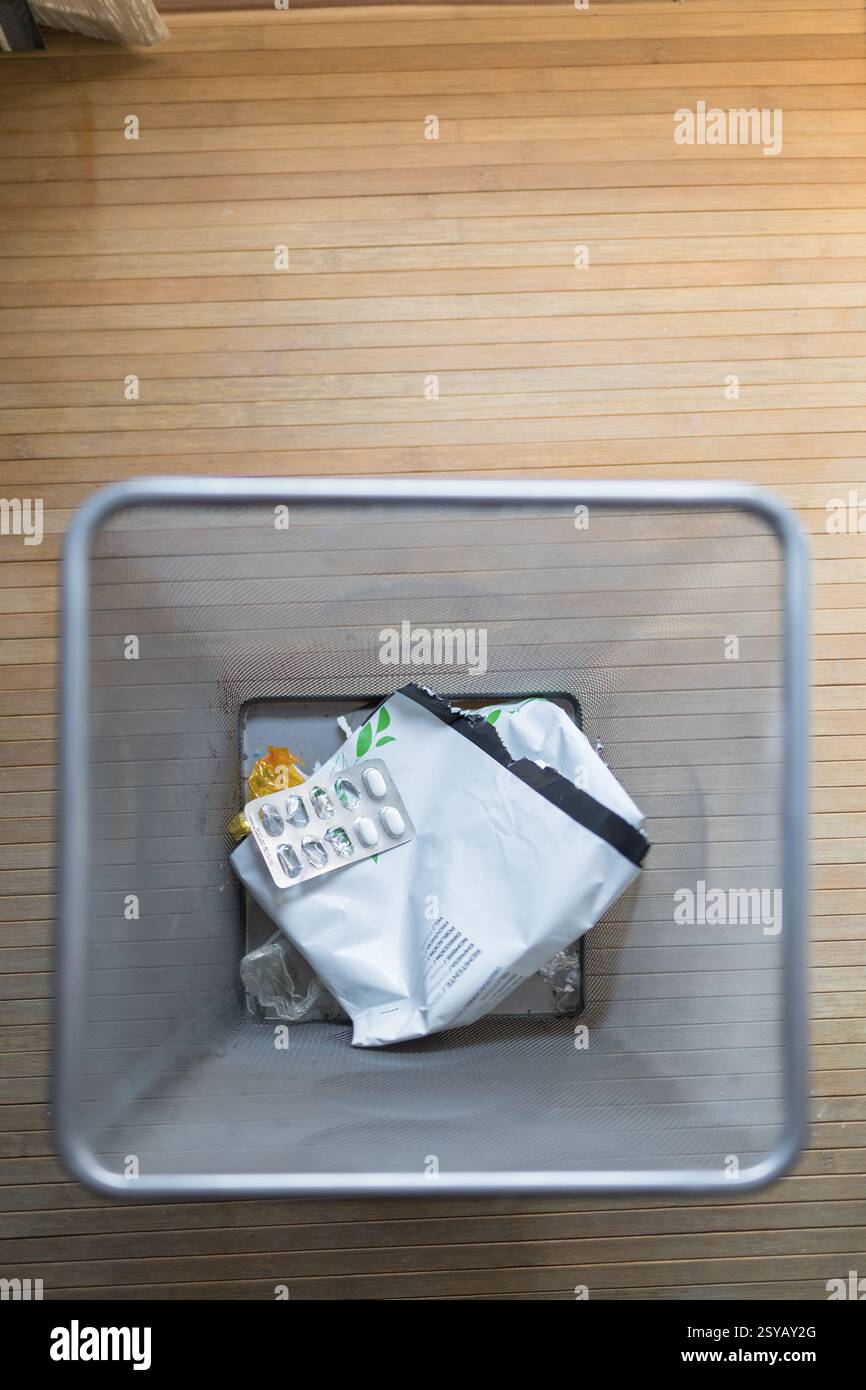 Eine Ansicht von oben nach unten auf einen Abfalleimer mit gebrauchten Pillenverpackungen und anderen Abfällen auf einem Holzboden. Dieses Bild zeigt die tägliche Abfallentsorgung im Haushalt Stockfoto