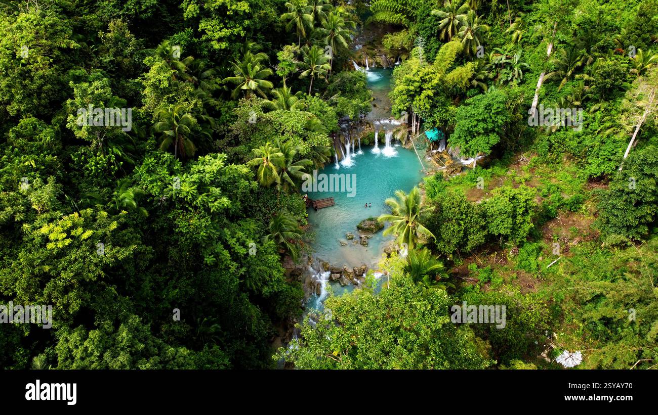 Ein Luftbild, das das üppige Grün und das lebhafte türkisfarbene Wasser eines abgeschiedenen tropischen Wasserfalls auf den Philippinen zeigt, ideal für Urlaube und Stockfoto