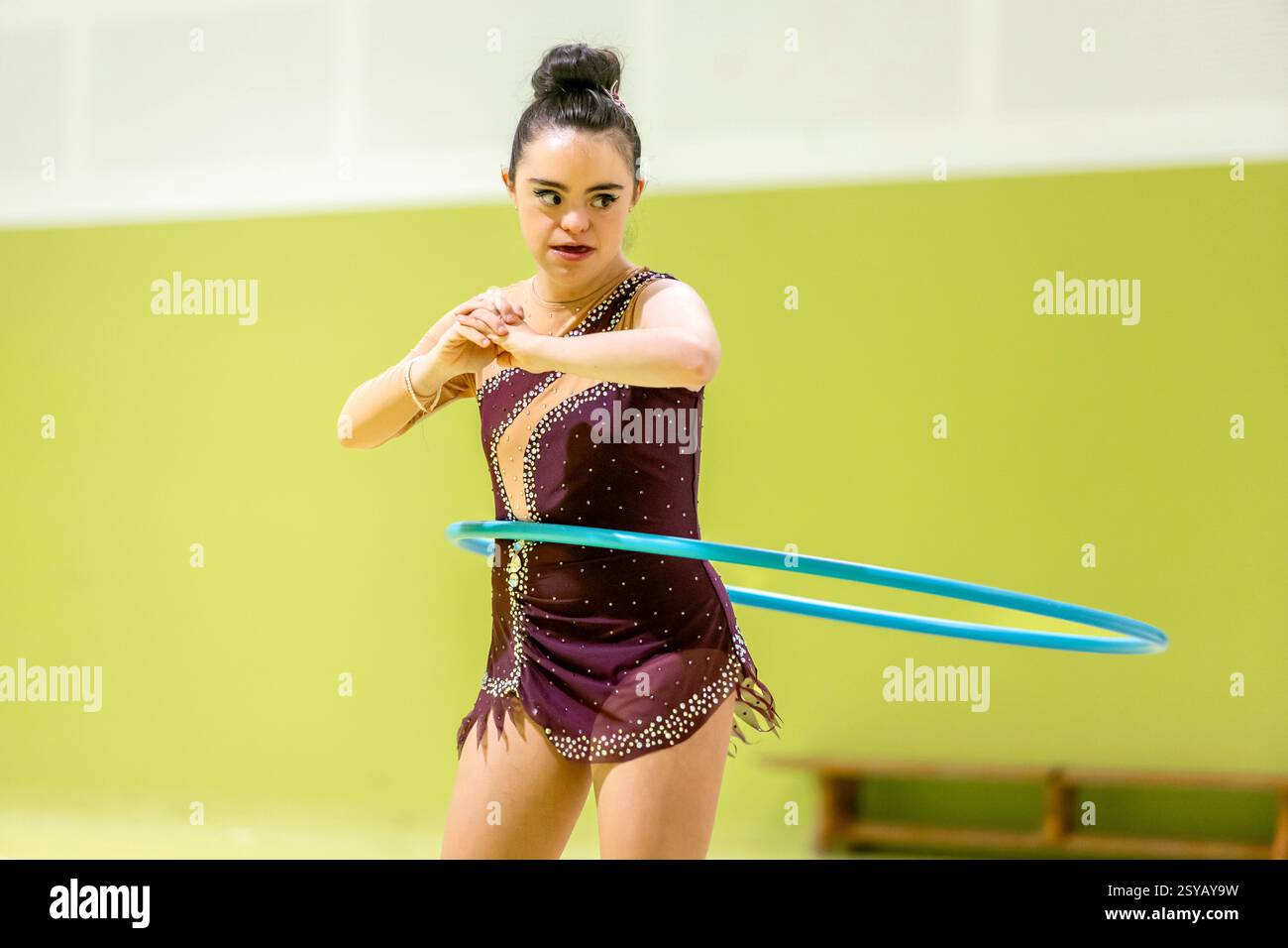 Eine behinderte rhythmische Turnerin tritt selbstbewusst mit einem Hula Hoop in einem hellen Innenraum auf und zeigt ihre Fähigkeiten und ihren Fokus. Sie trägt einen Glitzer, el Stockfoto