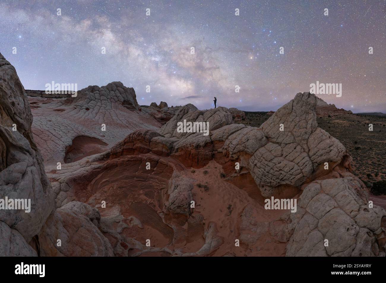 Ein weit entfernter, nicht erkennbarer Wanderer steht auf einer einzigartigen Felsformation in Utah, USA, unter einem sternenübersäten Himmel und zeigt die Schönheit eines Outdoor-Abenteuers Stockfoto