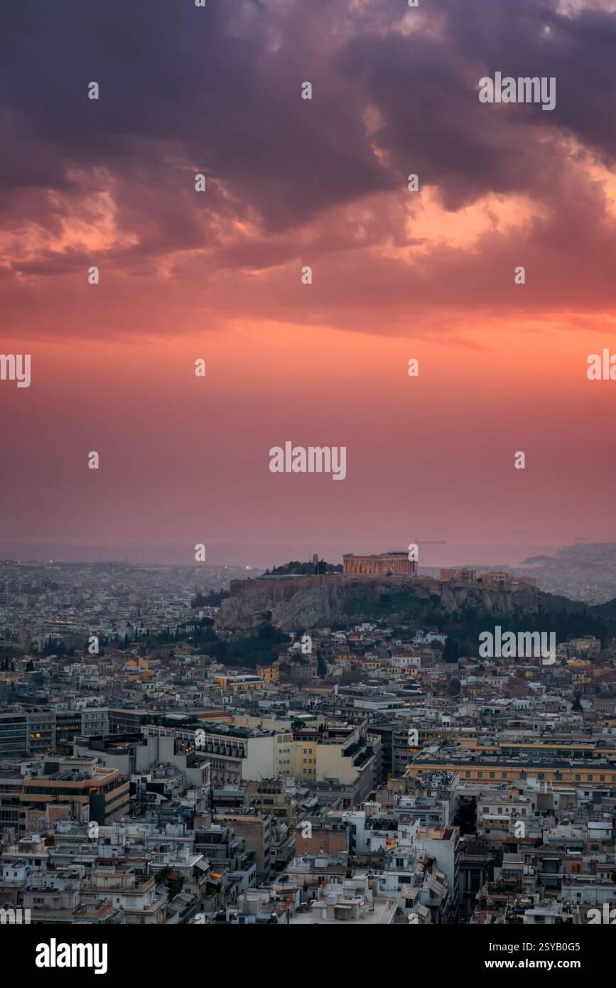 Ein atemberaubender Blick auf Athen bei Sonnenuntergang mit dem Parthenon und der Akropolis, die vor einem dramatischen Himmel beleuchtet werden. Das Stadtbild erstreckt sich bis zum h Stockfoto