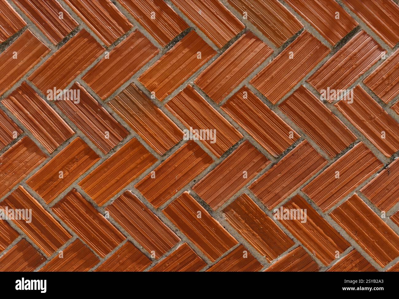 Ziegelwand mit klassischem Fischgrätenmuster. Die rot gefärbten Steine sind diagonal angeordnet und erzeugen einen dynamischen visuellen Effekt. Perfekt für Backgr Stockfoto