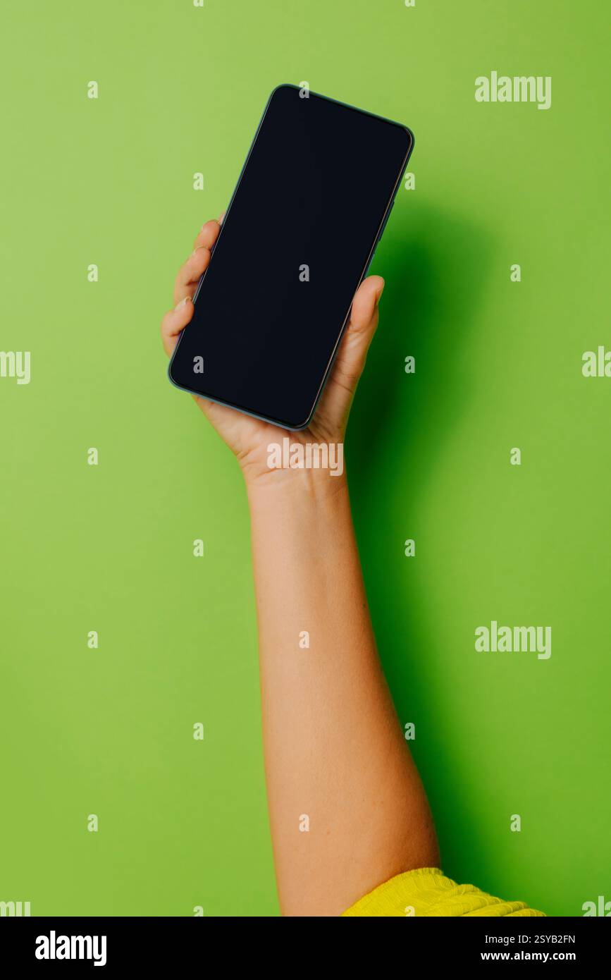 Die Hand einer anonymen Person, die ein Smartphone mit schwarzem Bildschirm vor grünem Hintergrund hält Stockfoto