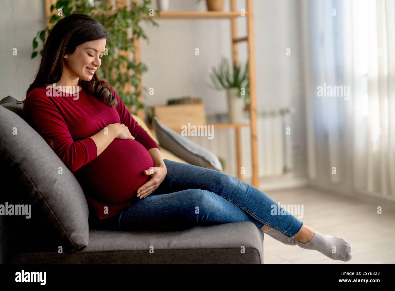 Schwangere Frau wird auf dem Bett ausgeruht gesehen. Sie wirkt zufrieden und gelassen und genießt einen ruhigen Moment Stockfoto