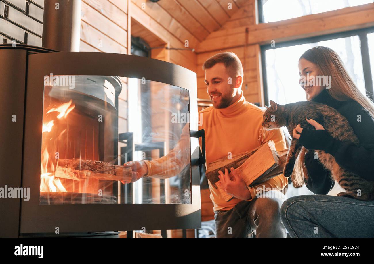 Ein Mann, der Holz in den Kamin legt. Die Frau sitzt mit einer niedlichen Katze. Stockfoto