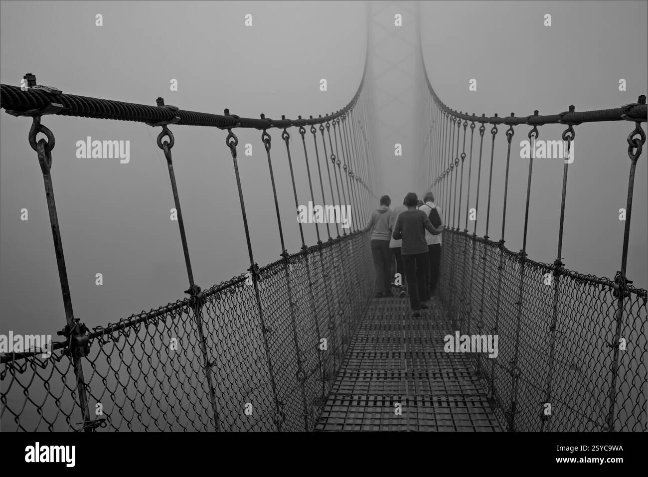 Chitwan National Park, Nepal - 6. Februar 2025 - Gruppe von Menschen überquert eine Brücke in niedrigen Wolken Stockfoto