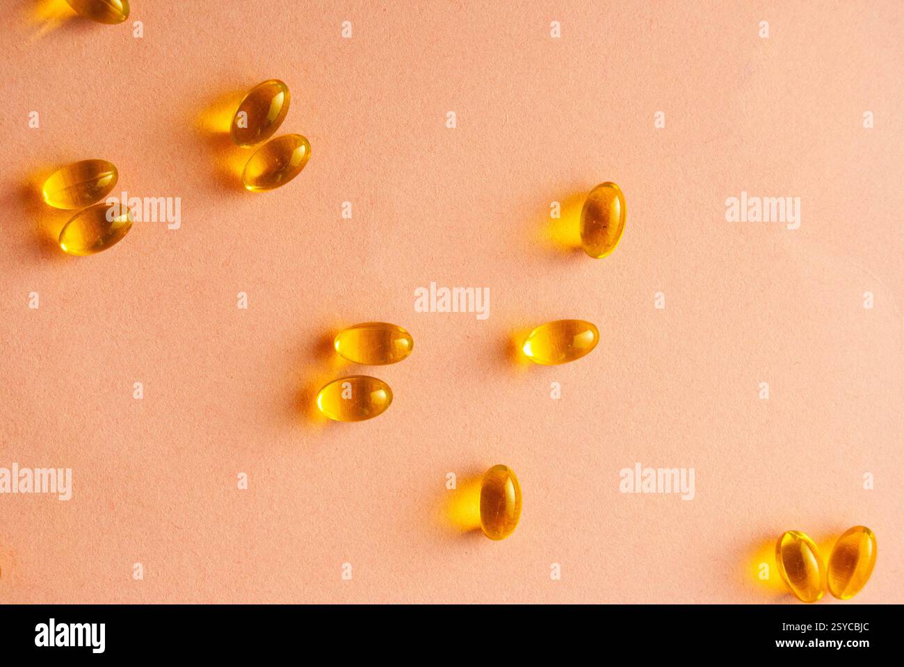 Goldene transparente Fischöl Omega-3-Pillen elegant angeordnet auf einem weichen rosa Hintergrund. Stockfoto
