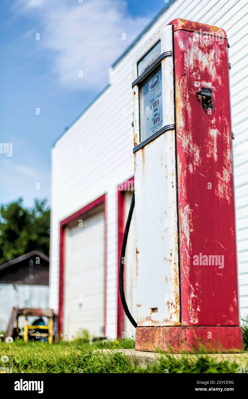 Rot-weiß-Tankstelle mit einer rostigen Pumpe. Die Pumpe ist alt und hat ein verblasstes Schild Stockfoto