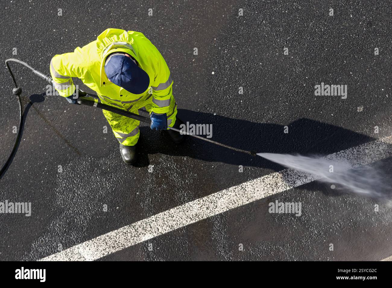 Straßenarbeiter tragen gut sichtbare Kleidung und reinigen Asphalt mit Hochdruckwasserstrahl. Hochwinkelansicht Stockfoto