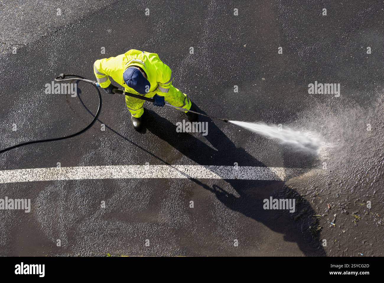 Straßenarbeiter tragen gut sichtbare Kleidung und reinigen Asphalt mit Hochdruckwasserstrahl. Hochwinkelansicht Stockfoto
