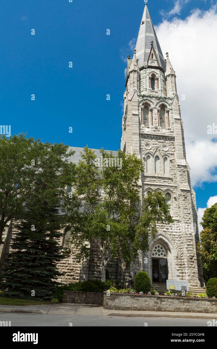 Große Steinkirche mit einem Kirchturm. Das Gebäude ist von Bäumen umgeben. Der Himmel ist blau und klar Stockfoto