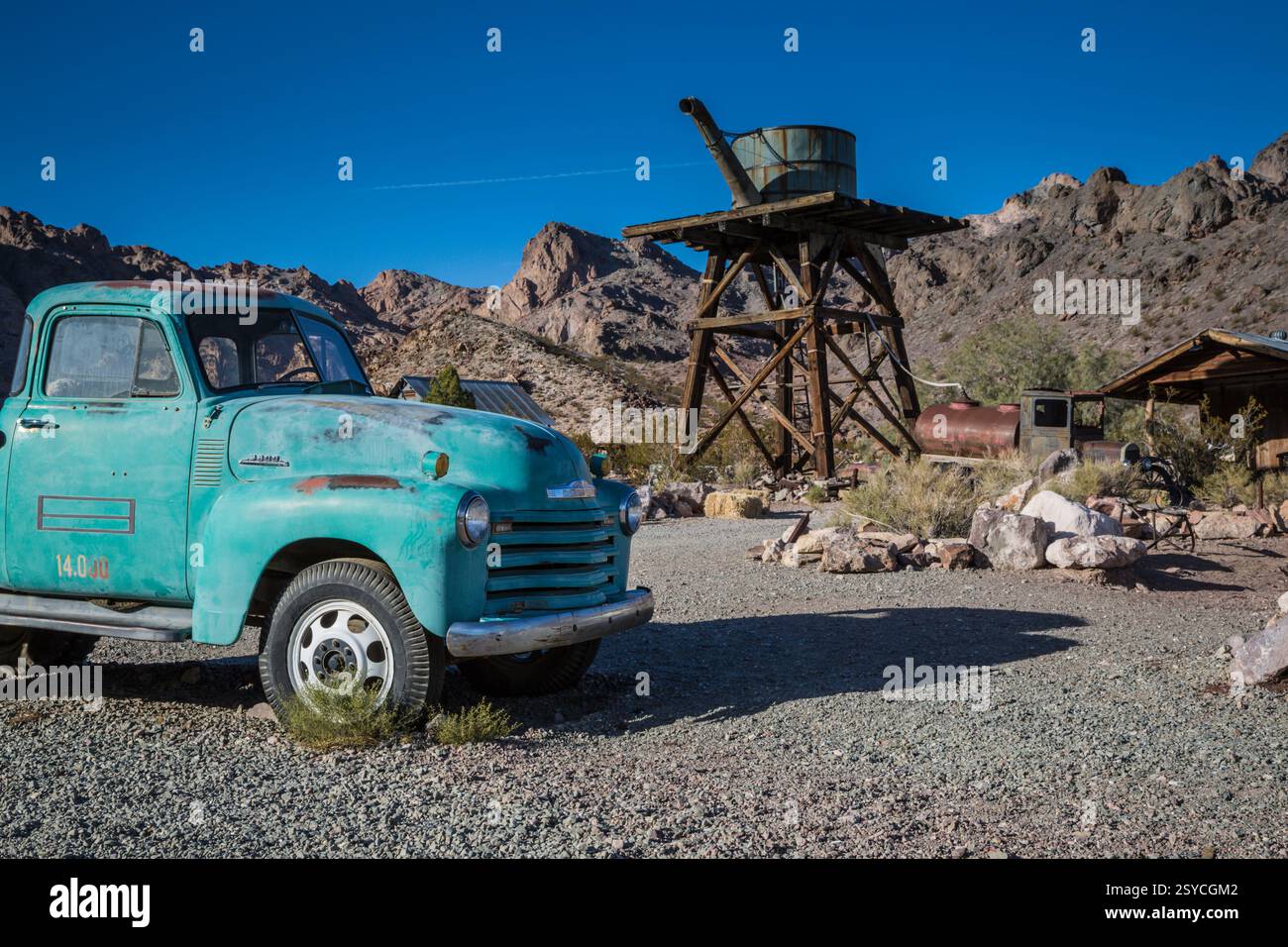 Blauer Truck parkt vor einem Gebäude. Der Truck ist alt und rostig. Das Gebäude besteht aus Holz Stockfoto
