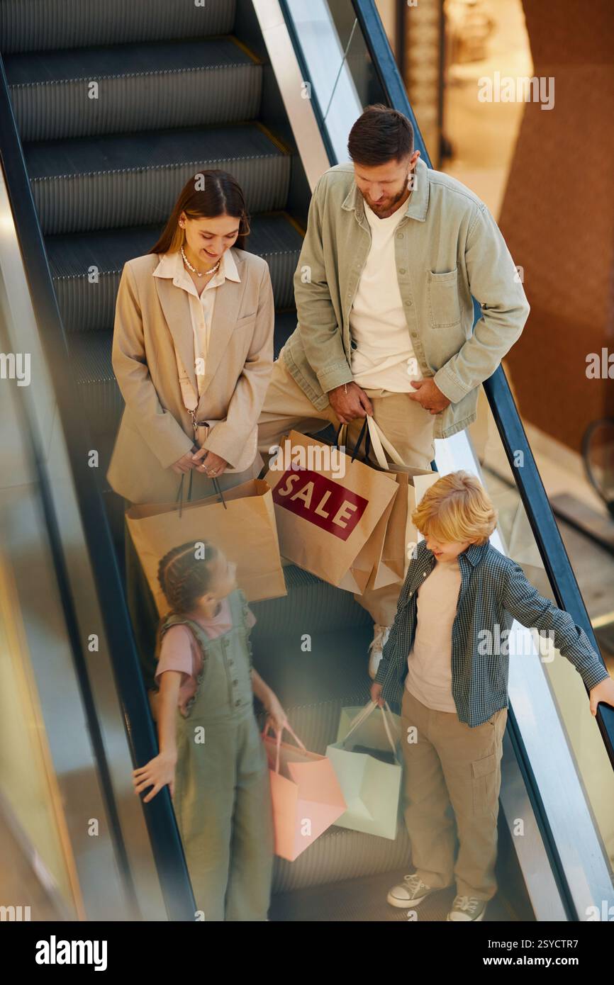 Vertikale Hochwinkelaufnahme der Familie mit riesigen Papiertüten in den Händen, die sich auf der Rolltreppe unterhalten, während sie hinuntergeht Stockfoto